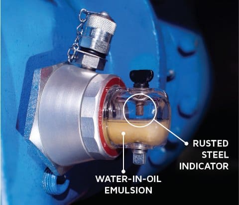 This sight glass makes the appearance of harmful levels of water easy to observe. The cloudiness of the oil indicates emulsified water, while the rust on the corrosion gauge punctuates the potential damage occurring to exposed internal machine surfaces.